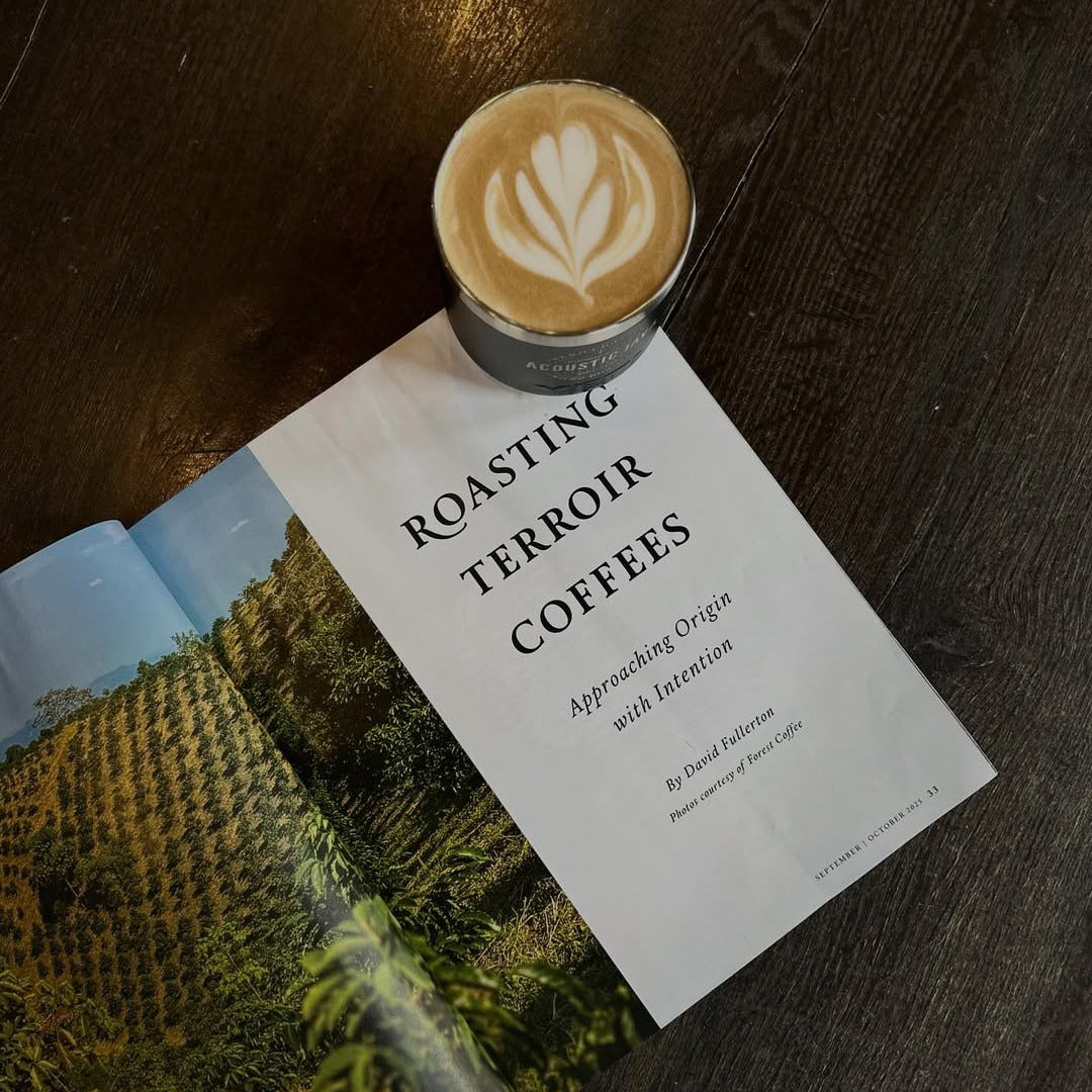 Cup of coffee with latte art on a magazine titled 'Roasting Terroir Coffees' on a wooden surface